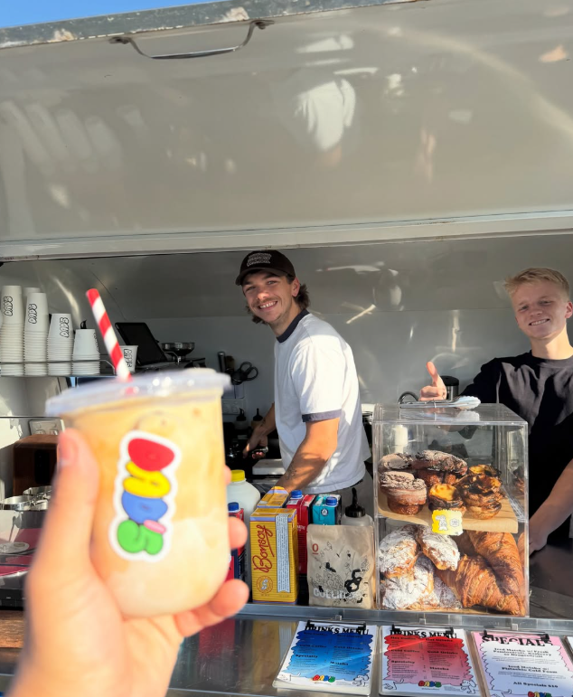 An iced drink held up at the Dad's trailer window, with two smiling baristas
