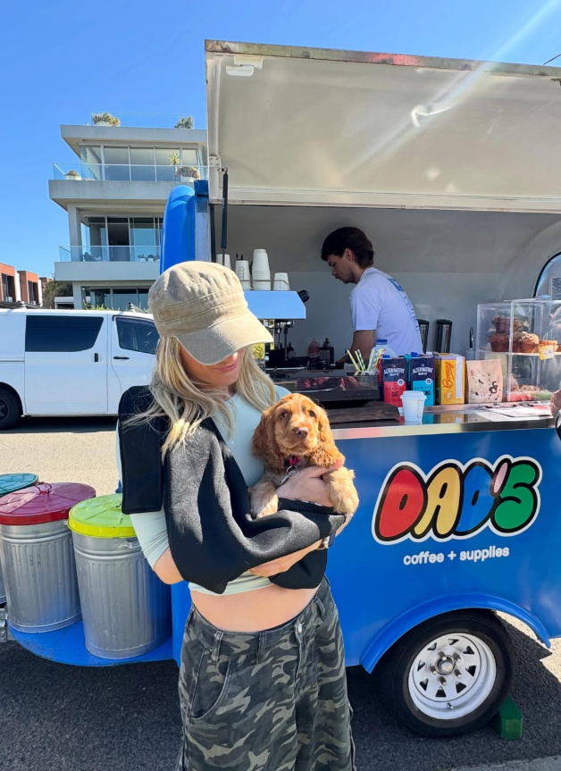 A woman holding a puppy in front of the blue Dad's coffee trailer