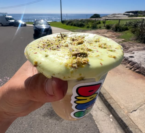 A Dad's cold brew with pistachio cold foam held up by the sea