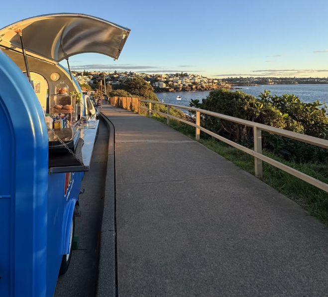 The blue Dad's trailer open beside a coastal walkway, with the ocean and houses behind